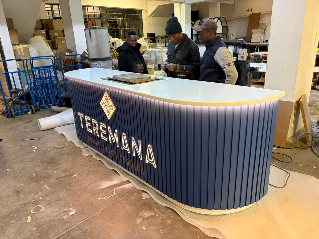 Three Steady Hand Studios crew members working together on the fluted Teremana counter in the workshop