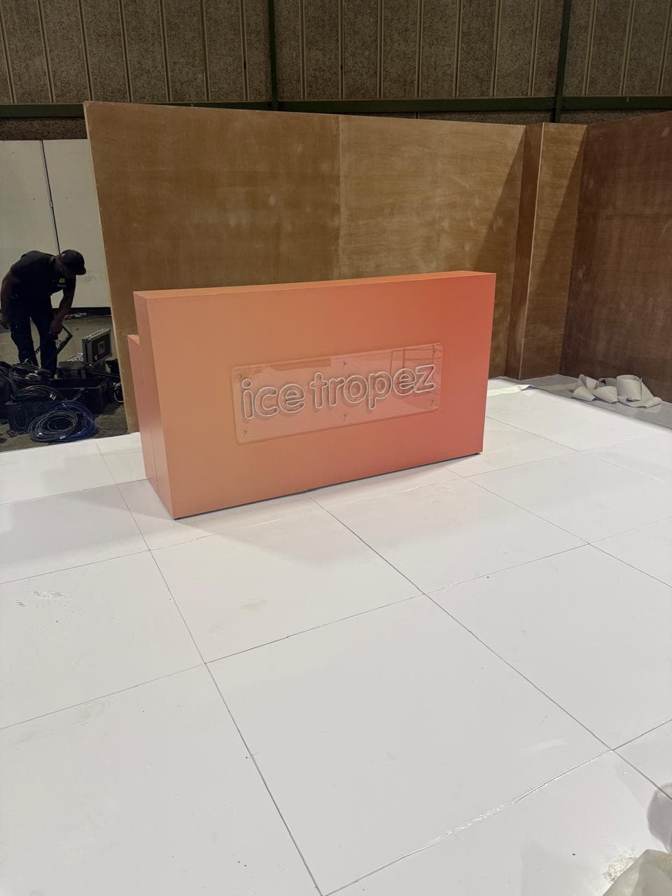 A minimal coral Ice Tropez counter with a debossed logo plaque, set up on a white-tiled event floor